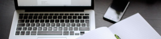Laptop, smartphone and notebook with pen lying on a table.