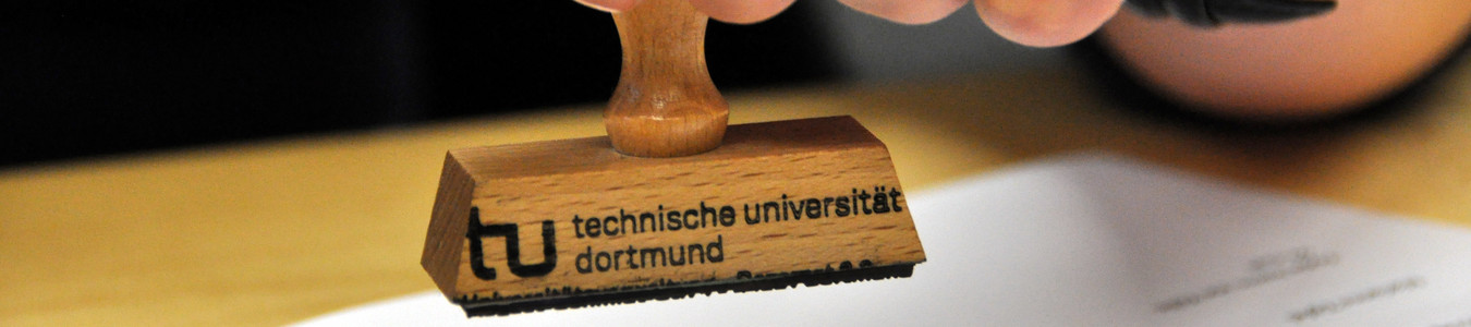 Nahufnahme eines TU Dortmund-Stempels über einem Blatt Papier
