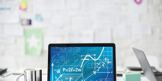 Ein Laptop mit mathematischen Formeln steht auf einem weißen Schreibtisch neben einer Tasse, Stiften und Blättern.