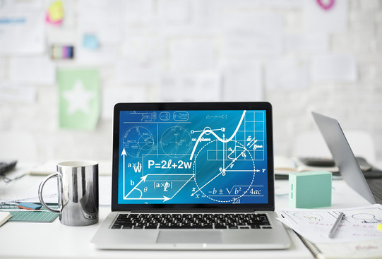 Laptop auf Tisch Ein Laptop mit mathematischen Formeln steht auf einem weißen Schreibtisch neben einer Tasse, Stiften und Blättern.
